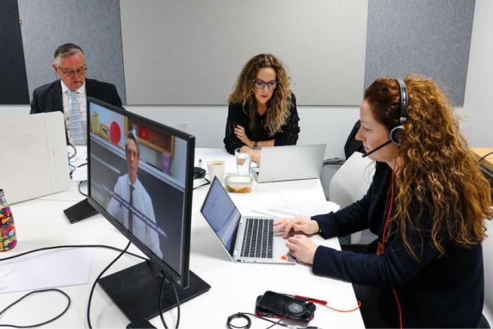 Photograph of 3 Techweek team members working at a large desk in front of their laptops.